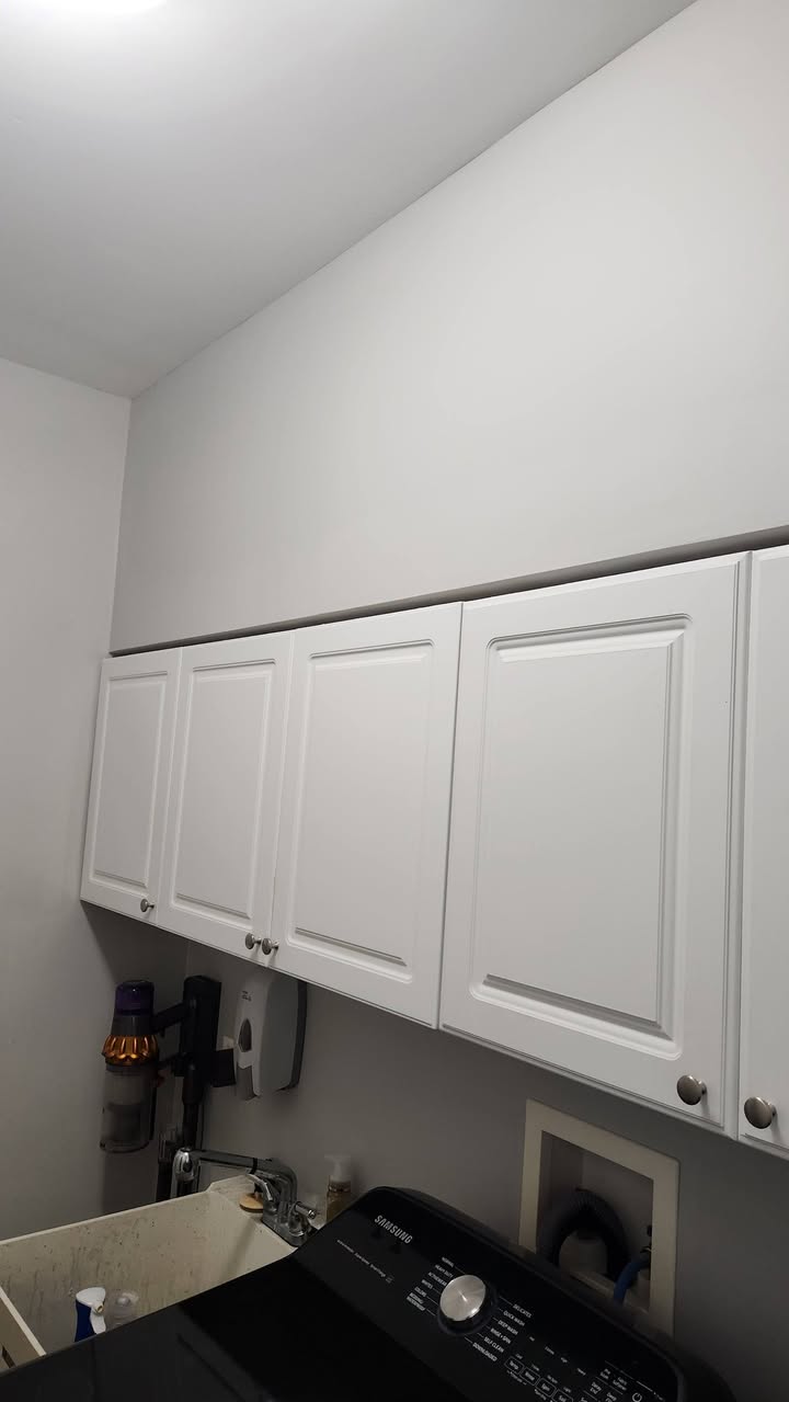 Detail of the refinished white laundry-room cabinetry against a clean grey wall.